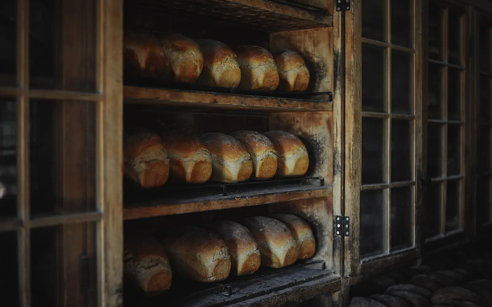 Rows of fresh loaves on the wooden shelves of a bakery rack
